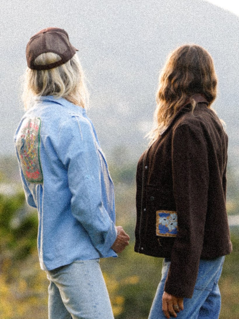 Two women from behind on a Marin hillside, one in a light denim shirt with an embroidered back panel, one in a brown jacket with a floral pocket patch